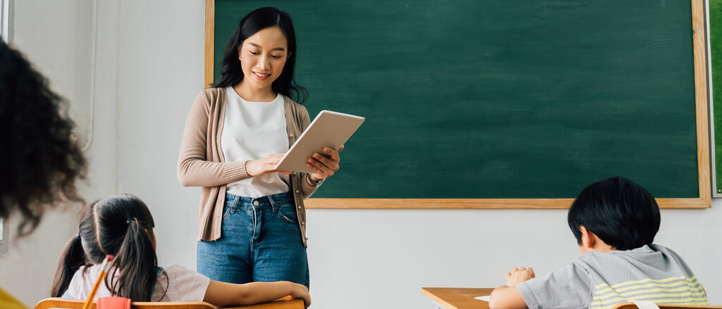 Ausbildungsgeräte Junge Lehrerin steht mit einem Tablet in der Hand vor ein paar Schülerinnen und Schülern