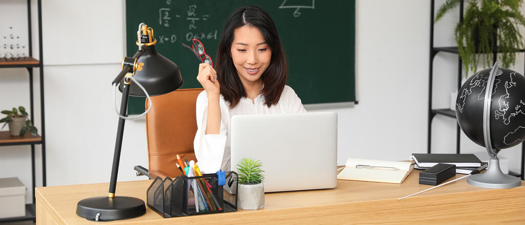 Lehrkraft mit Laptop Eine Lehrerin sitzt an ihrem Schreibtisch vor einem Laptop.